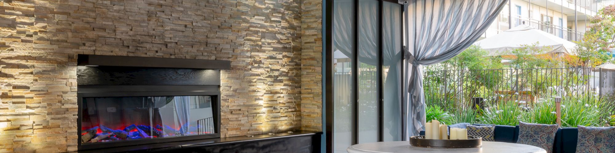 This image features a stylish outdoor seating area with a fireplace, wicker furniture, and pendant lights, creating a cozy, elegant atmosphere.